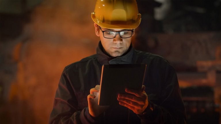 Homem com capacete amarelo e óculos de segurança olhando para o seu tablet