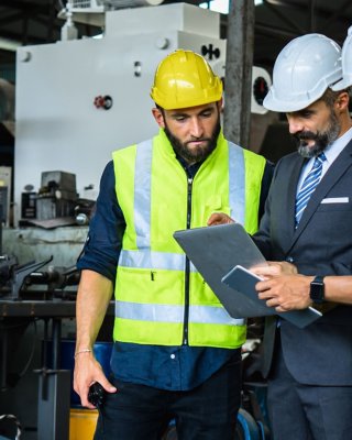 Industrial engineer with tablet and white hardhat and two workers in hardhats