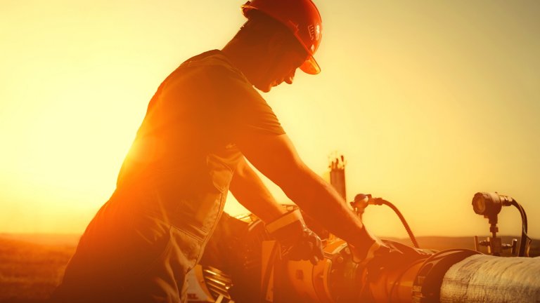 Oil worker is checking the oil pump on the sunset background.