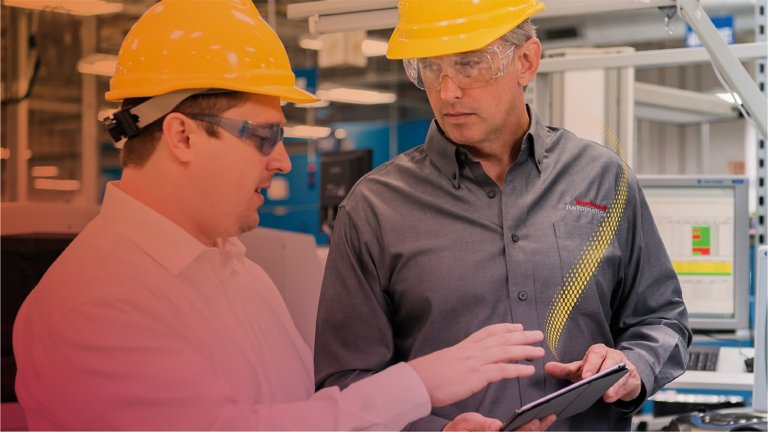 Two professionals wearing hard hats discussion operations with data on a smart tablet
