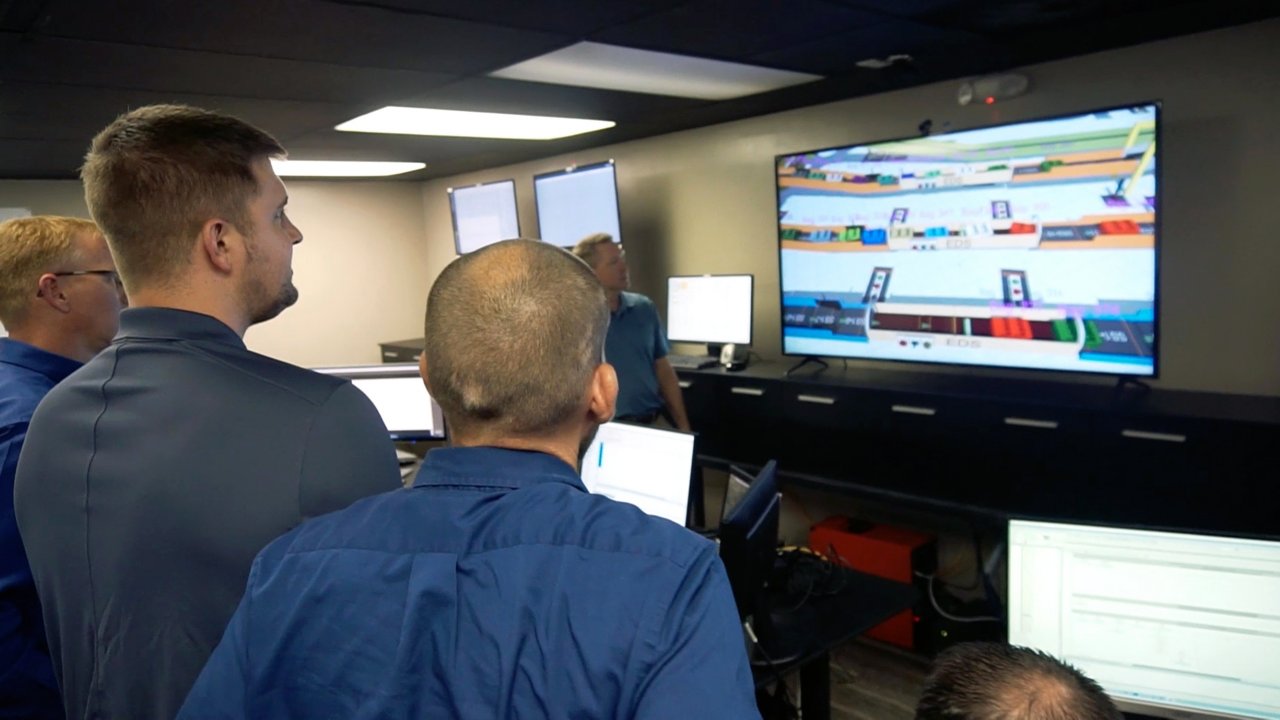 Engineers review baggage handling emulation on computer monitor.