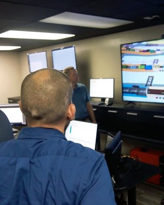 Engineers review baggage handling emulation on computer monitor.