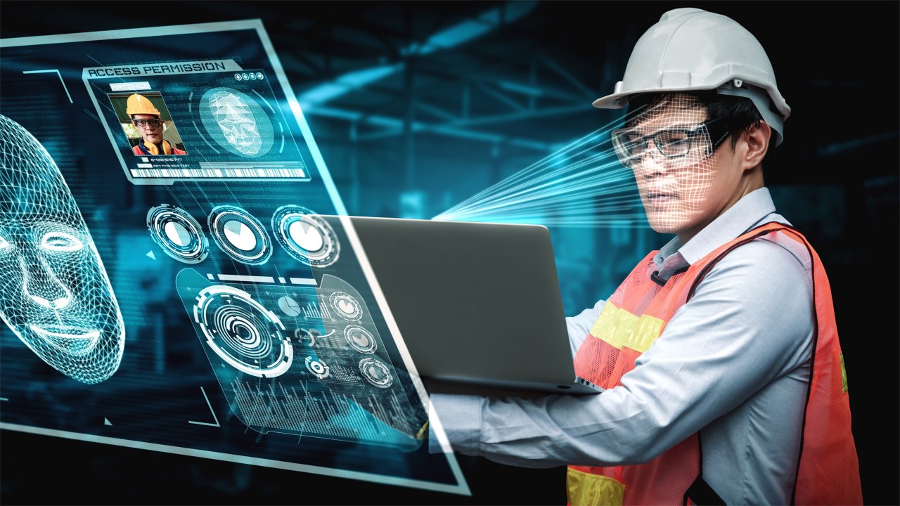 一位戴著安全帽與穿著橘色安全背心的男性正在製造廠中看著筆記型電腦。他所看的資訊就呈現在他的面前。