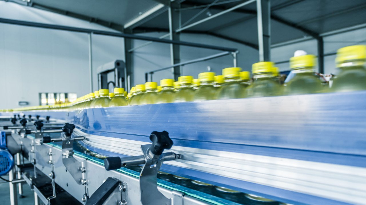 Una línea de botellas con tapas amarillas se mueven por un transportador en una planta