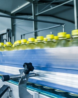 Linha de garrafas com tampas amarelas se movendo em um transportador em uma fábrica