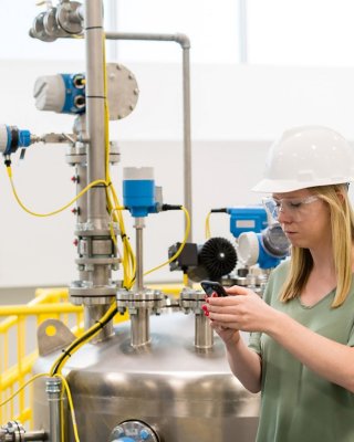 Female engineer in hard hat and holding a mobile device standing near a pump in a process manufacturing environment