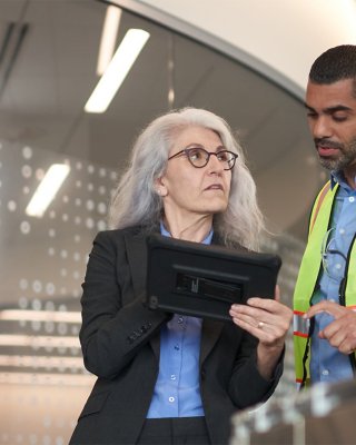 A woman explains cybersecurity details to an engineer within a manufacturing facility.