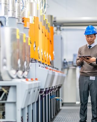 Two engineers using digital tablet while examining manufacturing machinery in factory