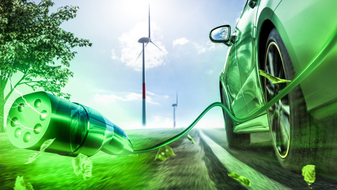 Green electric vehicle driving down road with the vehicle charging cable trailing behind