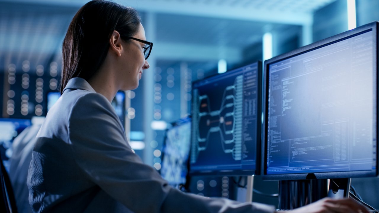 Female employee with glasses sitting beside a coworker in a technical area viewing software on her monitor