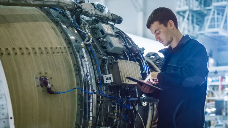 Un empleado con chaqueta azul introduce información en su tableta dentro de una planta