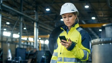 Une femme portant un casque de protection blanc et regardant un téléphone