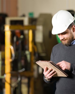 Man holding tablet device and looking at equipment on production floor