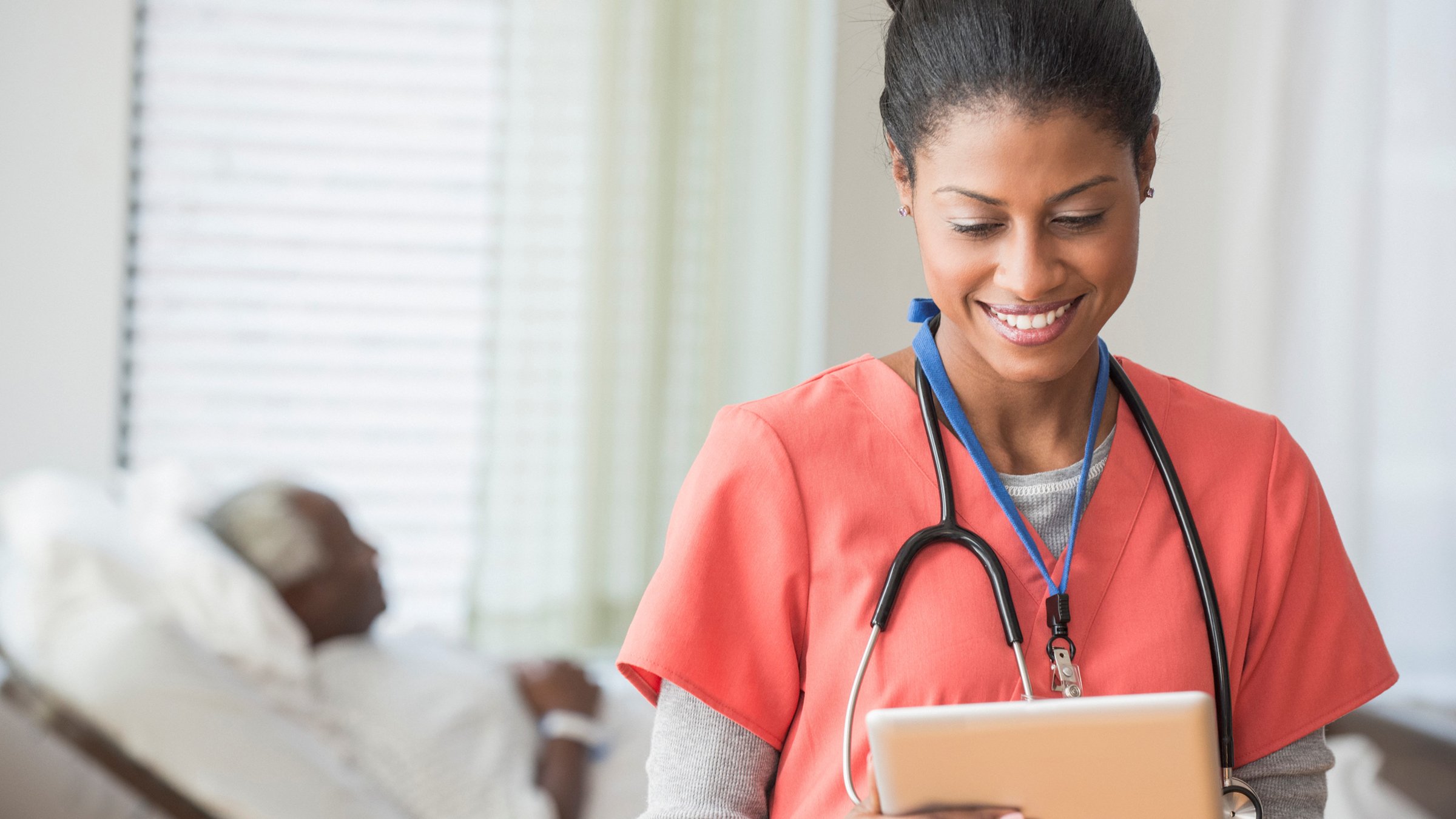 Female care provider wearing scrubs and a stethoscope looking at a tablet