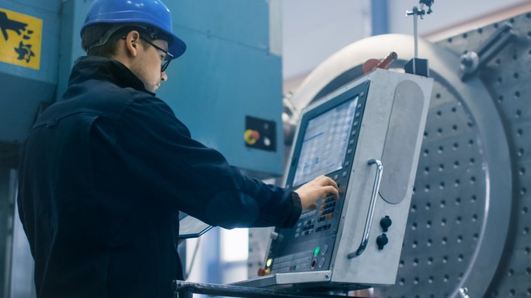 Empleado de sexo masculino en una fábrica; de pie e ingresando información en una pantalla táctil para una máquina