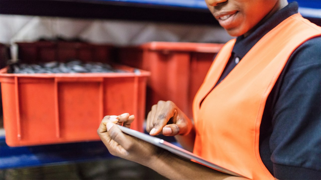 Employee viewing her tablet beside a conveyor with parts in bins