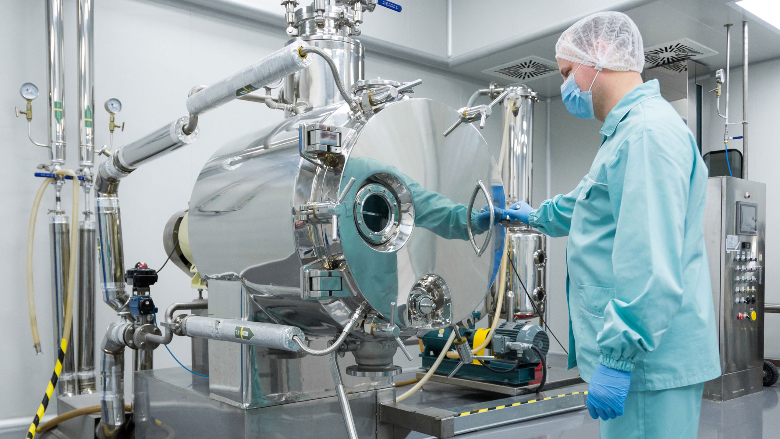 Employé de biopharmaceutique utilisant un équipement industriel et portant un vêtement de protection bleu, une charlotte blanche et un masque