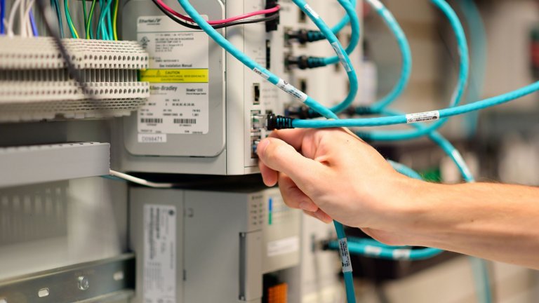 La mano de un trabajador de IT conectando un cable Ethernet a un switch Stratix de Rockwell Automation