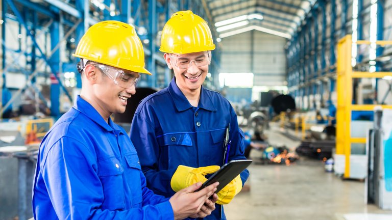 Dois funcionários sorridentes em uma fábrica olhando informações em um tablet