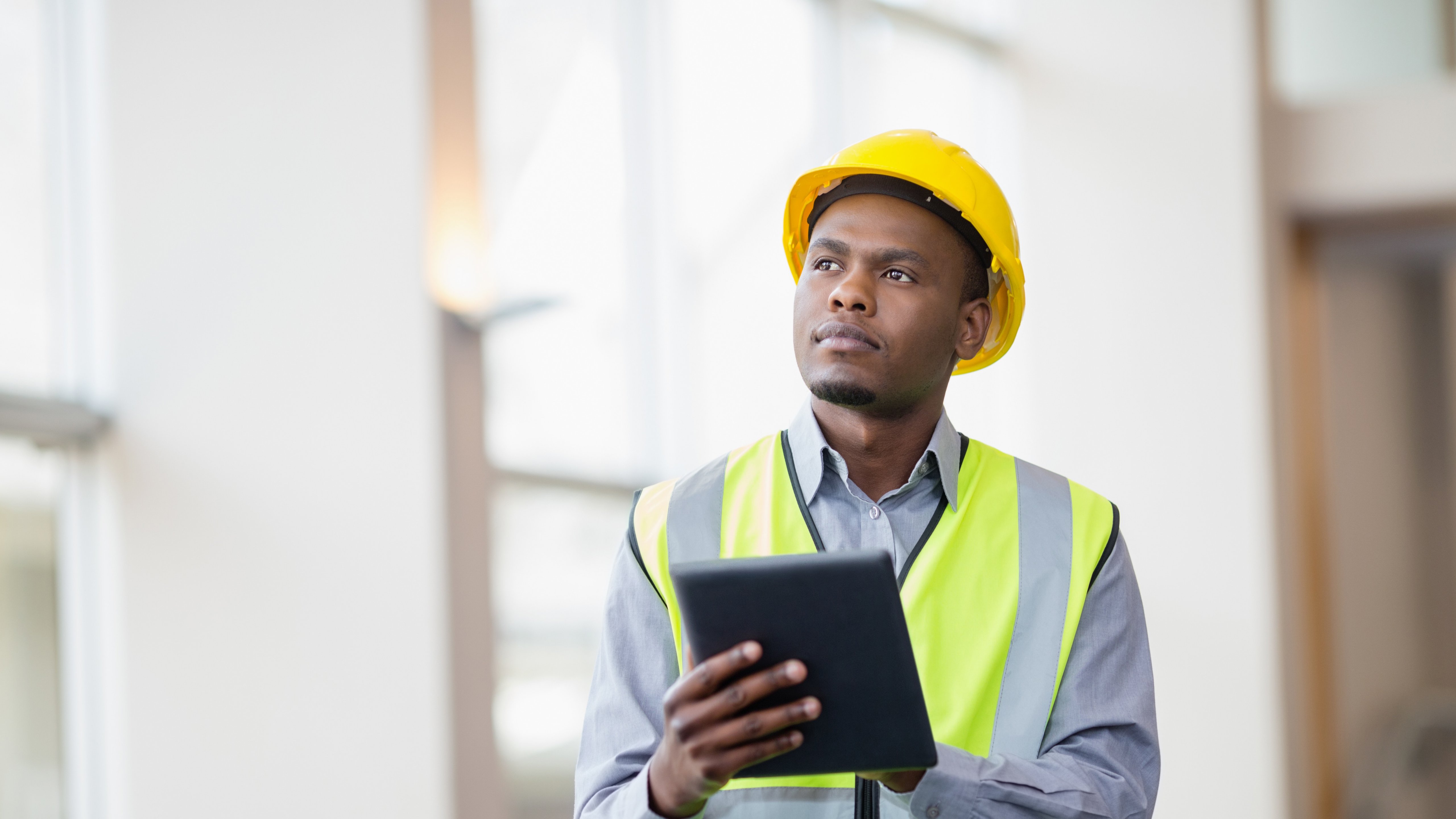 Maintenance engineer wearing yellow hard hat checking preventive maintenance data outside factory.