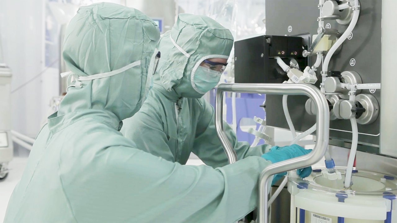 Two life sciences professionals in protective gear set up single-use equipment in a modern production facility.
