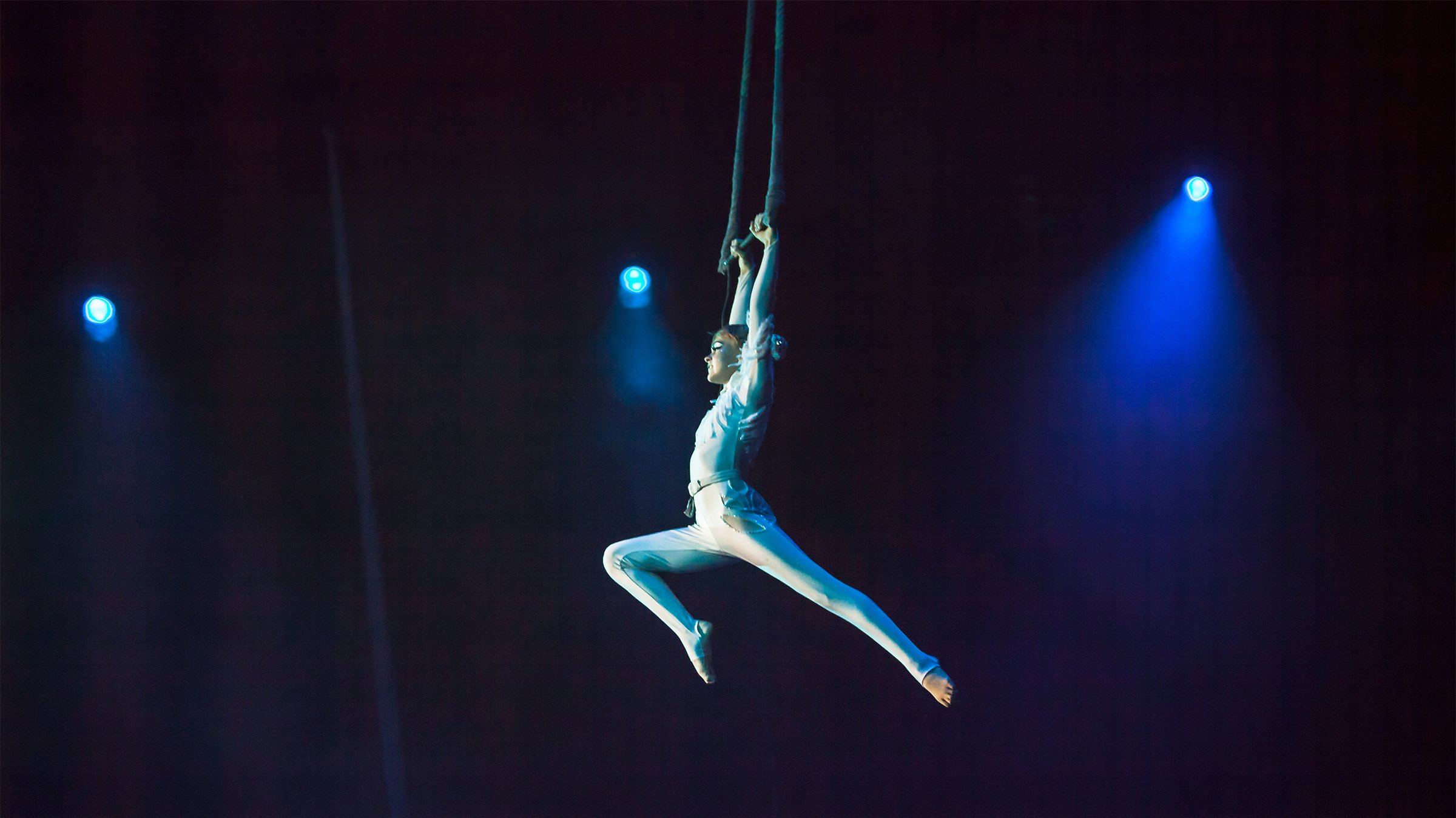 Acrobat swinging on stage with blue stage lights