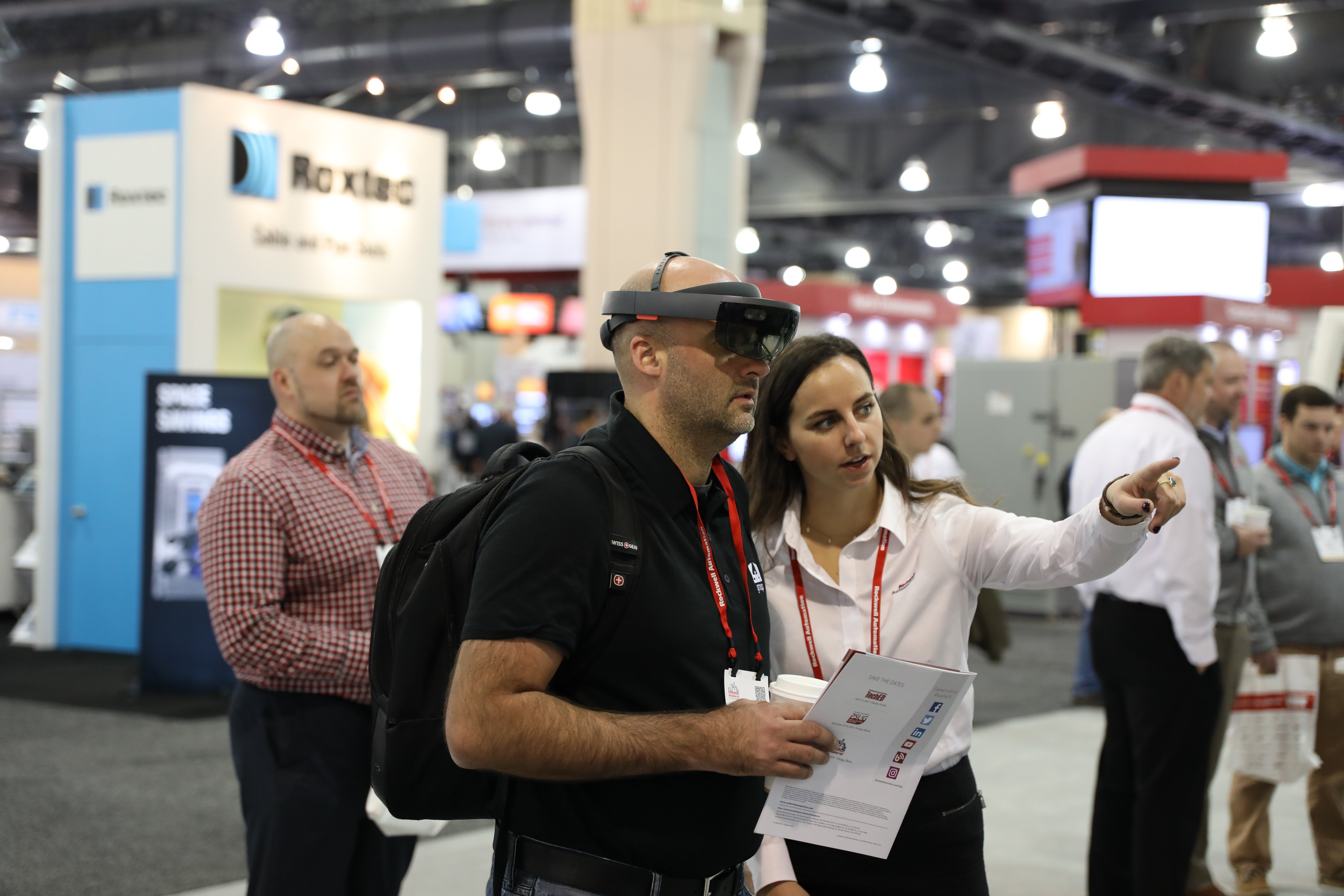 Two people on show floor at Automation Fair discussing AR technology, one wearing AR headset.