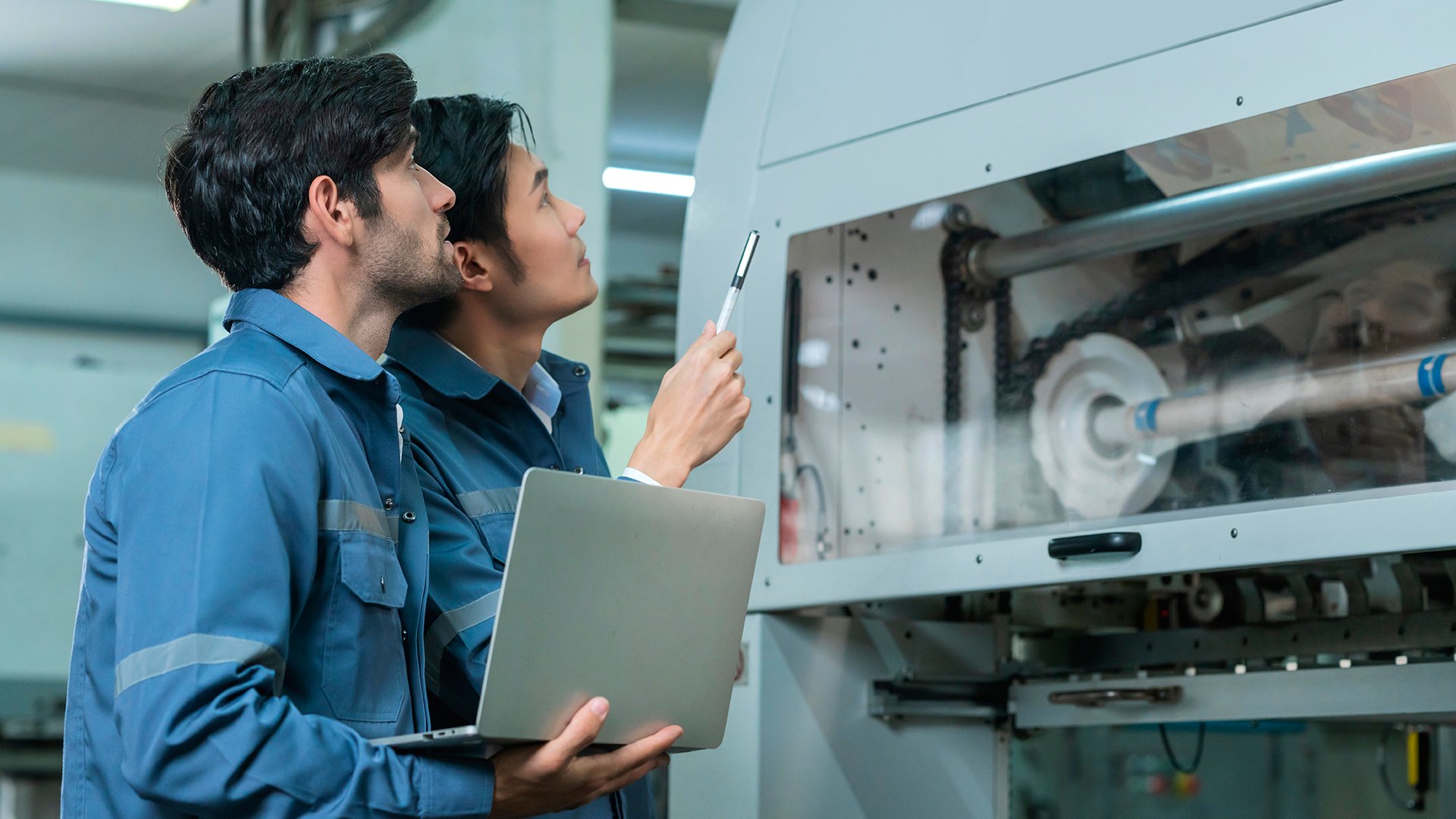 Male Asian caucasian engineer professional having a discussion standing consult at machine in the factory ,two expert coworker brainstorm explaining and solves the process of the cnc operate machine