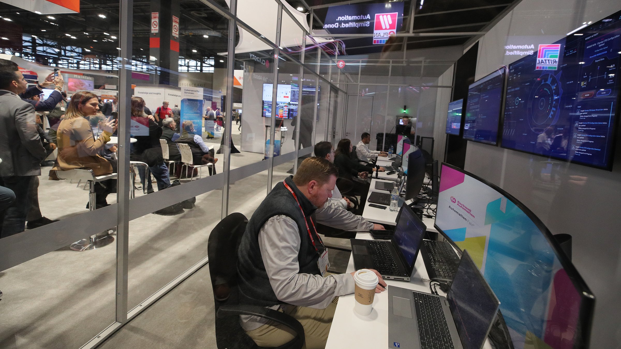 Attendees at Automation Fair look into the Cyber Ops Center at people looking at monitors