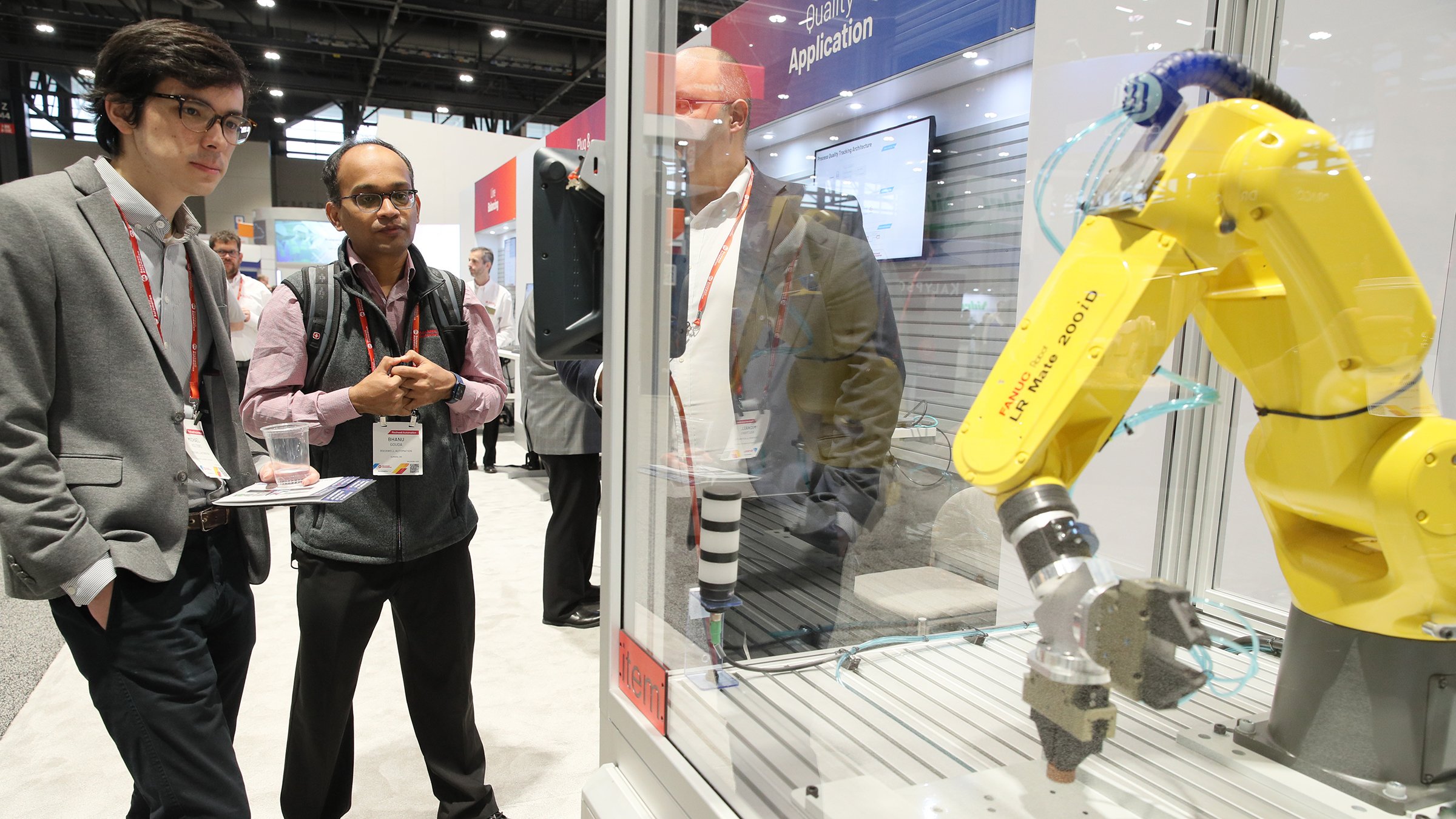 Three people looking at robot arm display on show floor at Automation Fair 2022