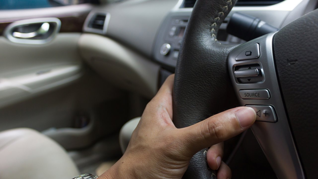 Man's finger pushing a speaker volume button on a car steering wheel