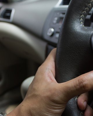 Man's finger pushing a speaker volume button on a car steering wheel