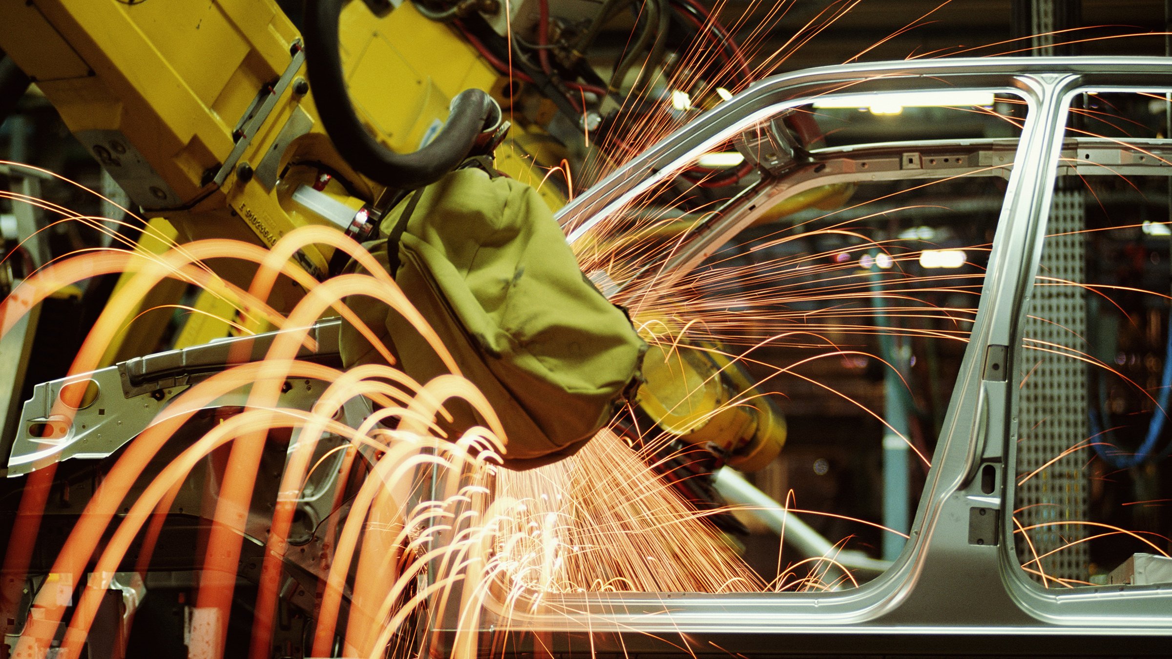 Sparks flying from a yellow robotic welding arm in an automotive factory