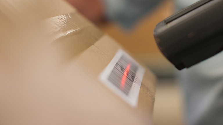 Bar code scanning gun in a manufacturing warehouse scanning a bar code sticker on a box