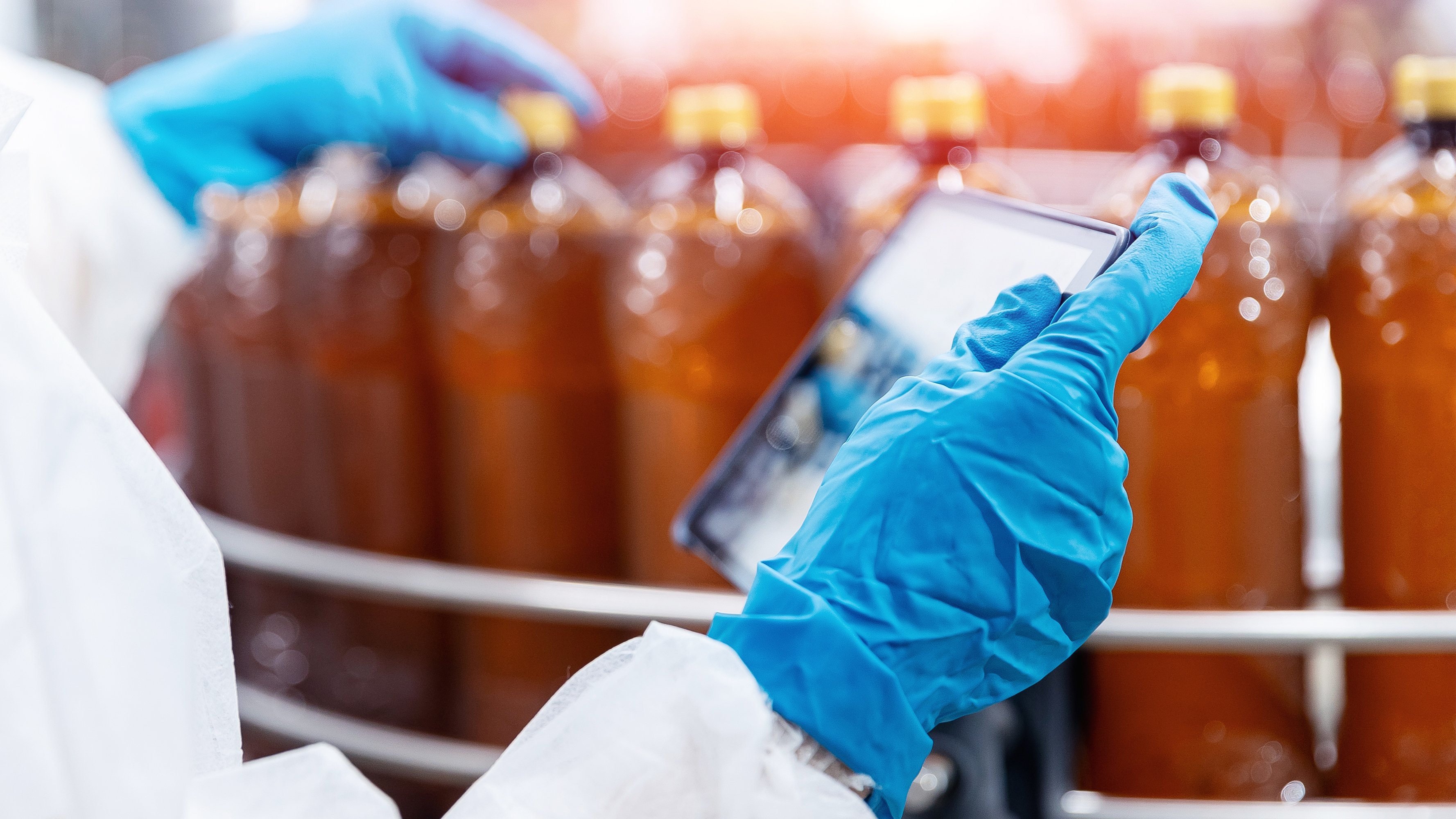Factory worker inspecting production line with brown plastic beer bottles on Brewery plant with computer tablet