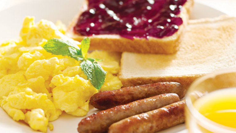 Breakfast that includes a plate with scrambled eggs, sausage and toast served with orange juice
