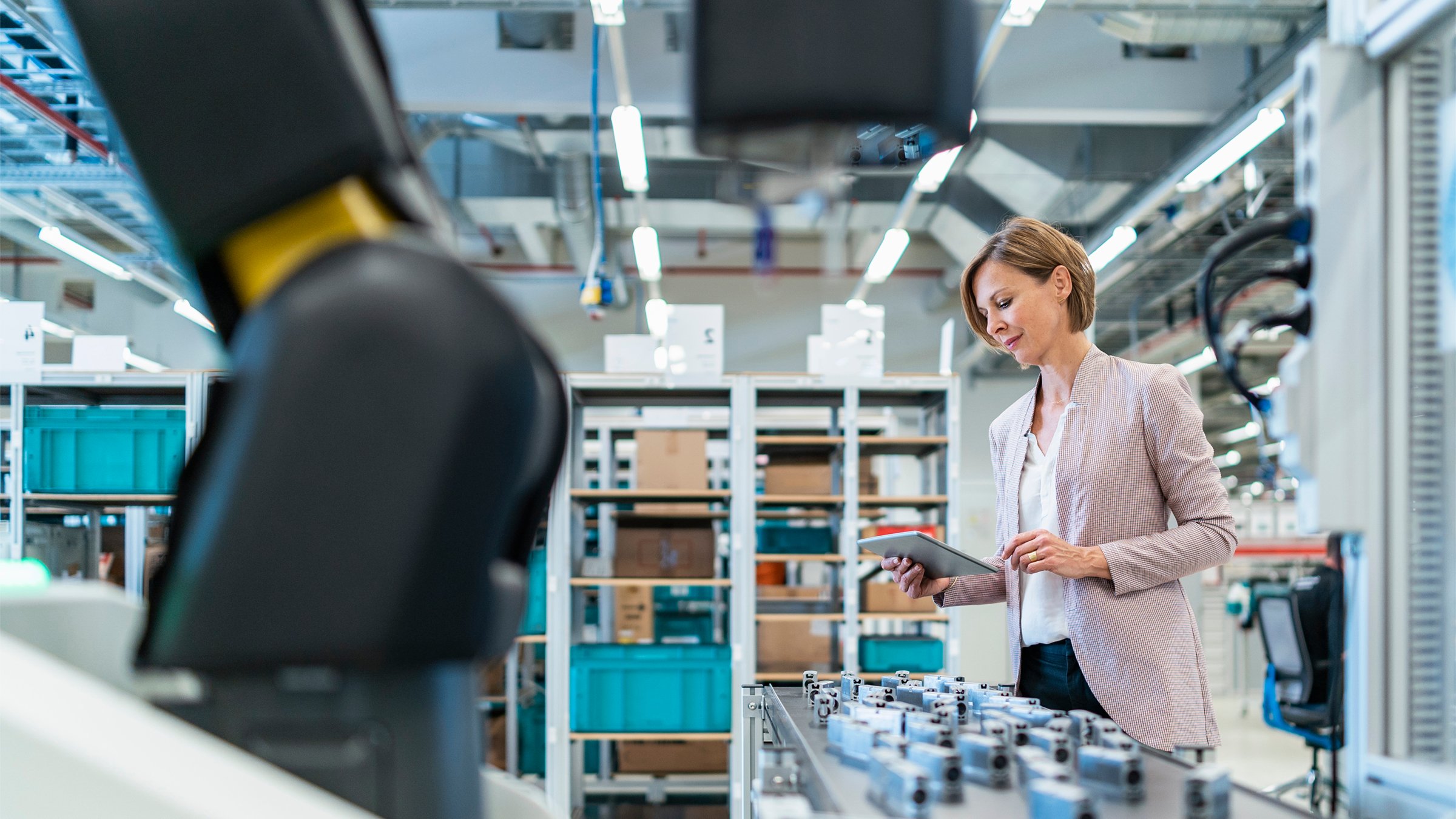 Businesswoman holding and viewing a tablet in a modern factory with machinery