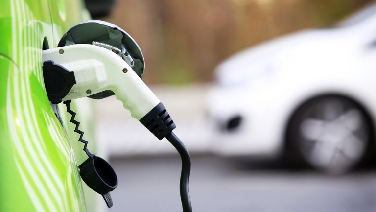 Close up view of charging cable connected to a bright green electric vehicle. Another electric vehicle in the blurred background.