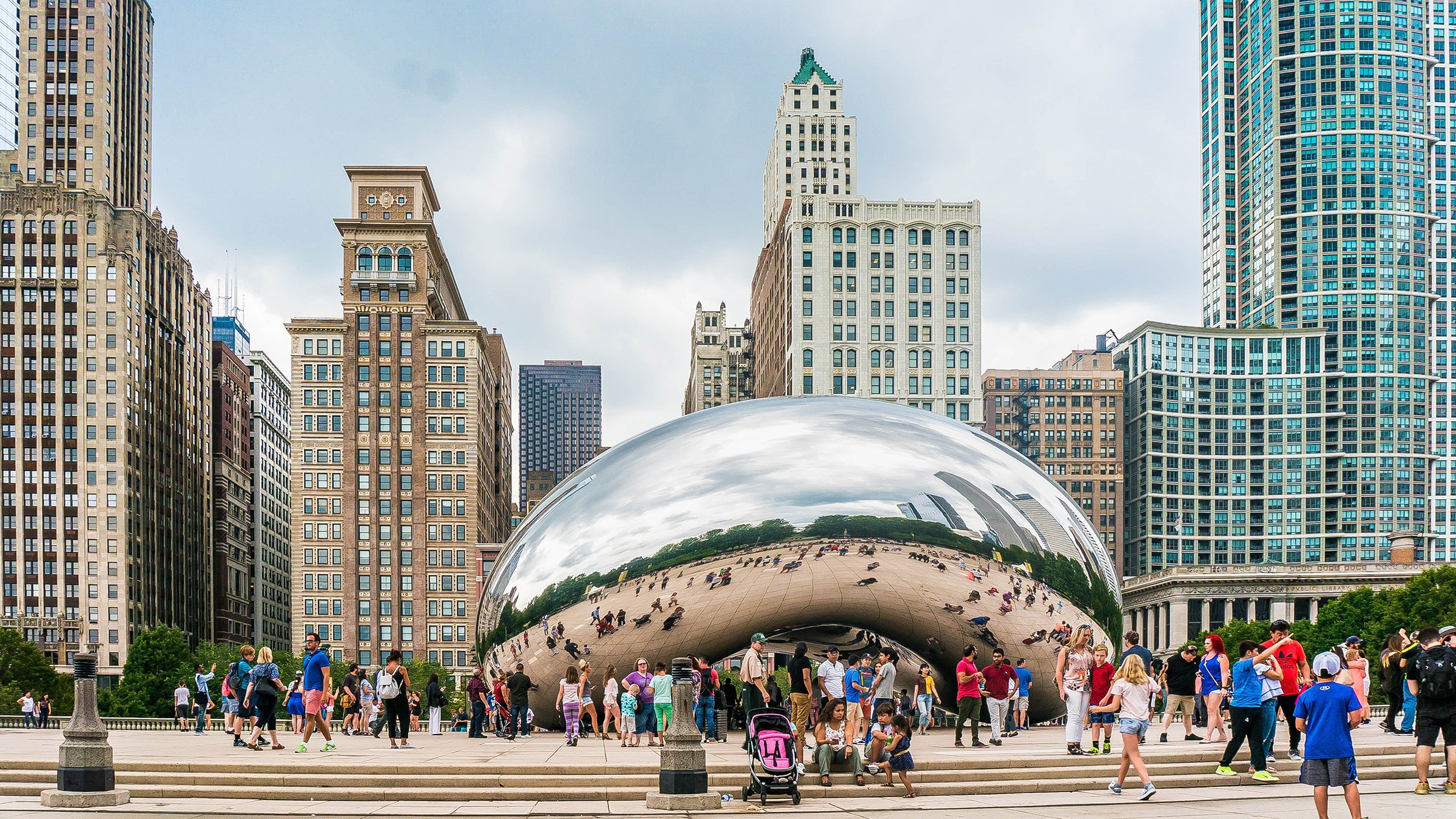 Cloud Gate, aka The Bean in Chicago IL USA Millennium Park with buildings in background with Bean in the center of the photo and many people in the pictue during the day.
