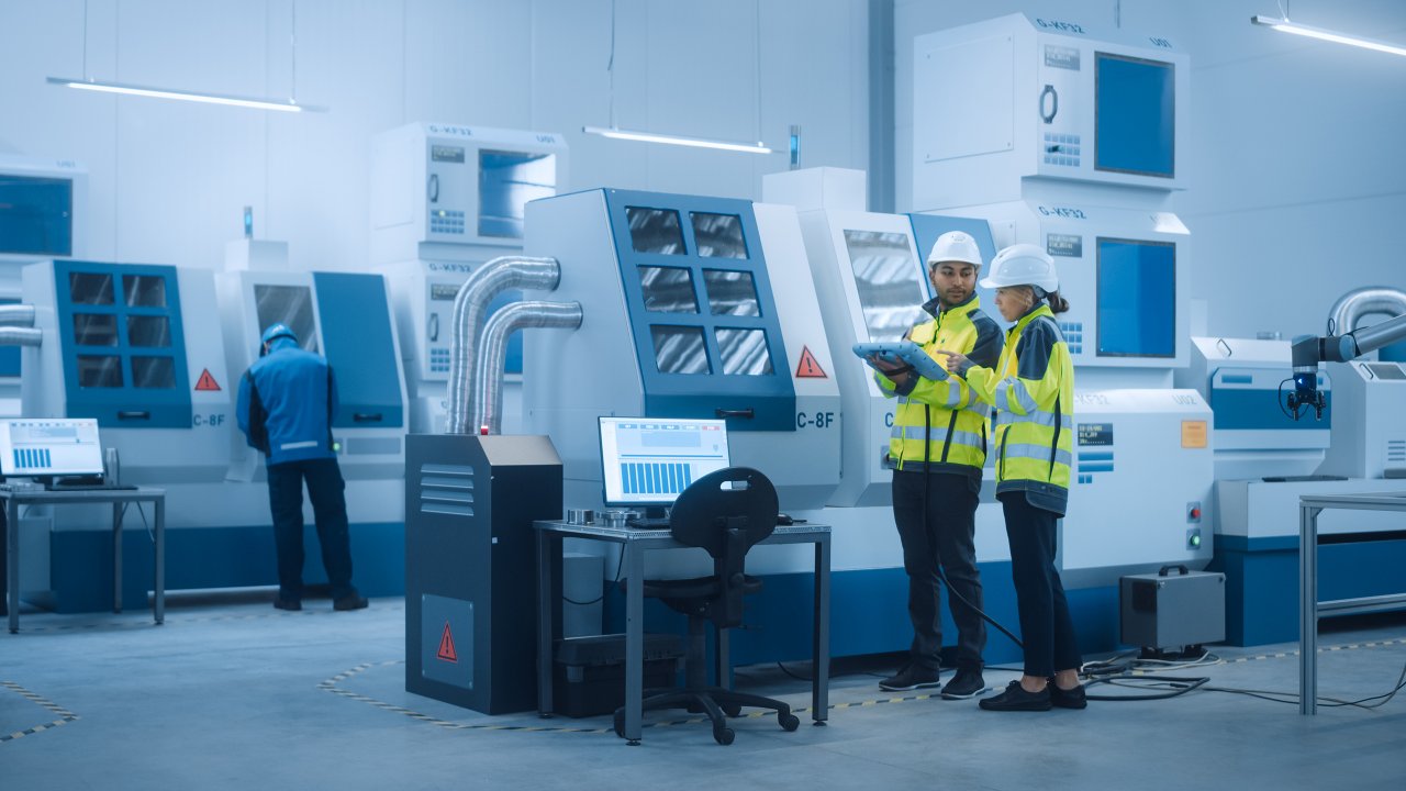 总工程师和项目经理穿戴着安全背心和安全帽，在工厂使用数字平板电脑控制器。