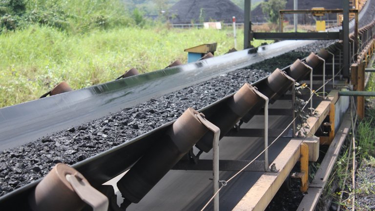 Industrial Machine conveyor belt moving large amounts of coal on mining site.