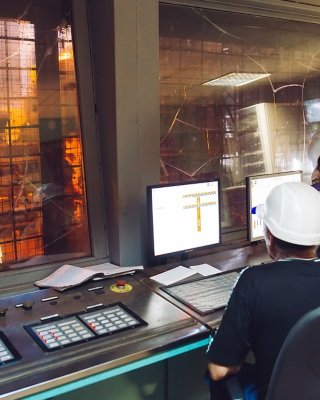 Dos personas con casco blanco mirando los monitores en una sala de control sobre una acería