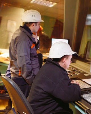 Funcionários na mesa usando capacetes, visualizando o chão de fábrica e o software em seus laptops