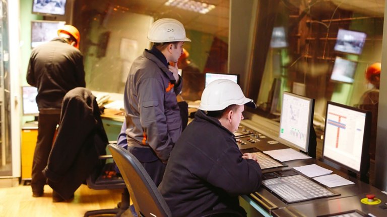Empleados con casco en sus escritorios observando la planta y el software en sus computadoras portátiles