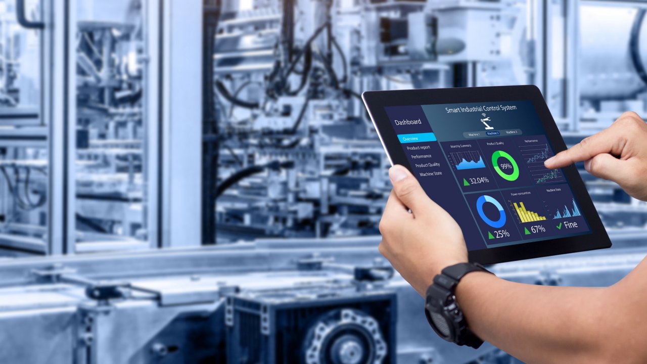 Smart industry control concept.Hands holding tablet on blurred automation machine as background Close up view of technician’s hands holding a tablet showing analytics in a factory in front of white robotic arm.