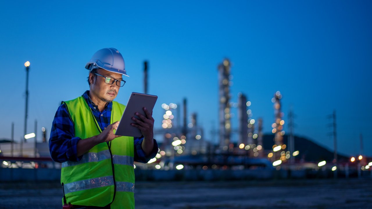 Ingeniero con uniforme de seguridad y casco mirando tablet con fábrica de refinería de petróleo en el fondo