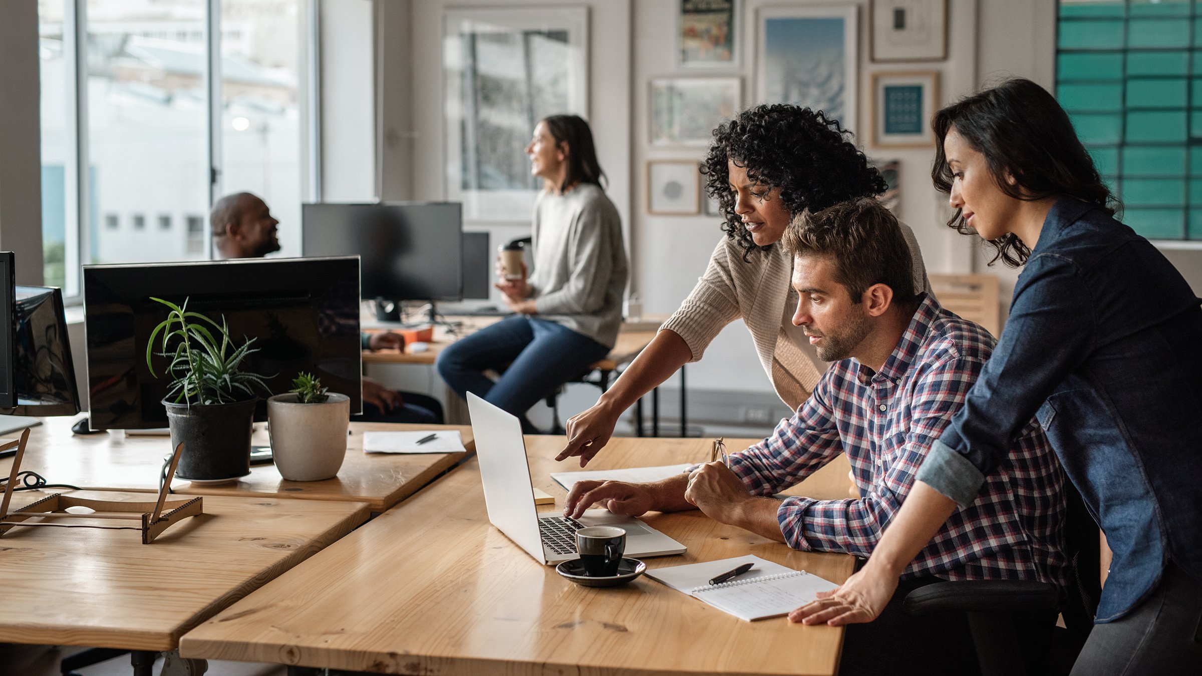 Group of diverse young employees collaborating on a laptop at their office desk