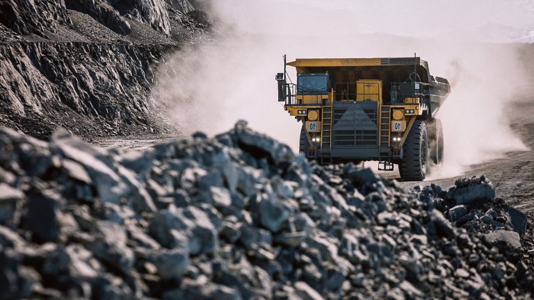 Un camion-benne se dirige vers le champ de mines à ciel ouvert, de gros fragments de roche apparaissent au premier plan.