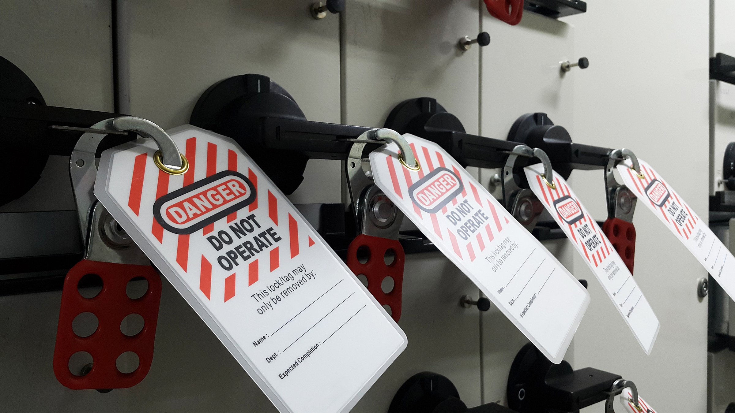 Row of industrial electrical panels with lockout/tagout tags and safety first point. 