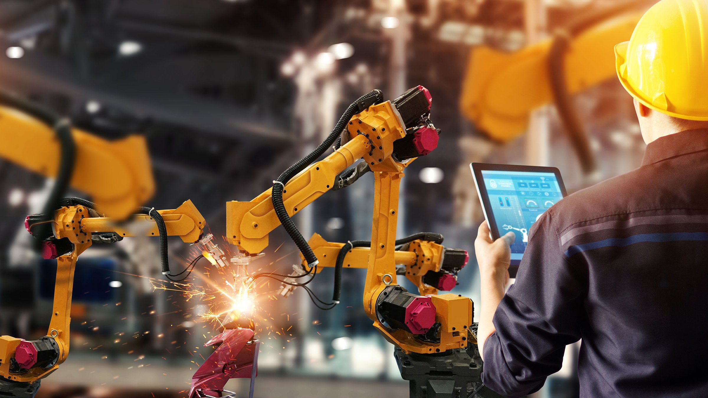 Male engineer checks and controls yellow, robotic welding equipment in intelligent factory